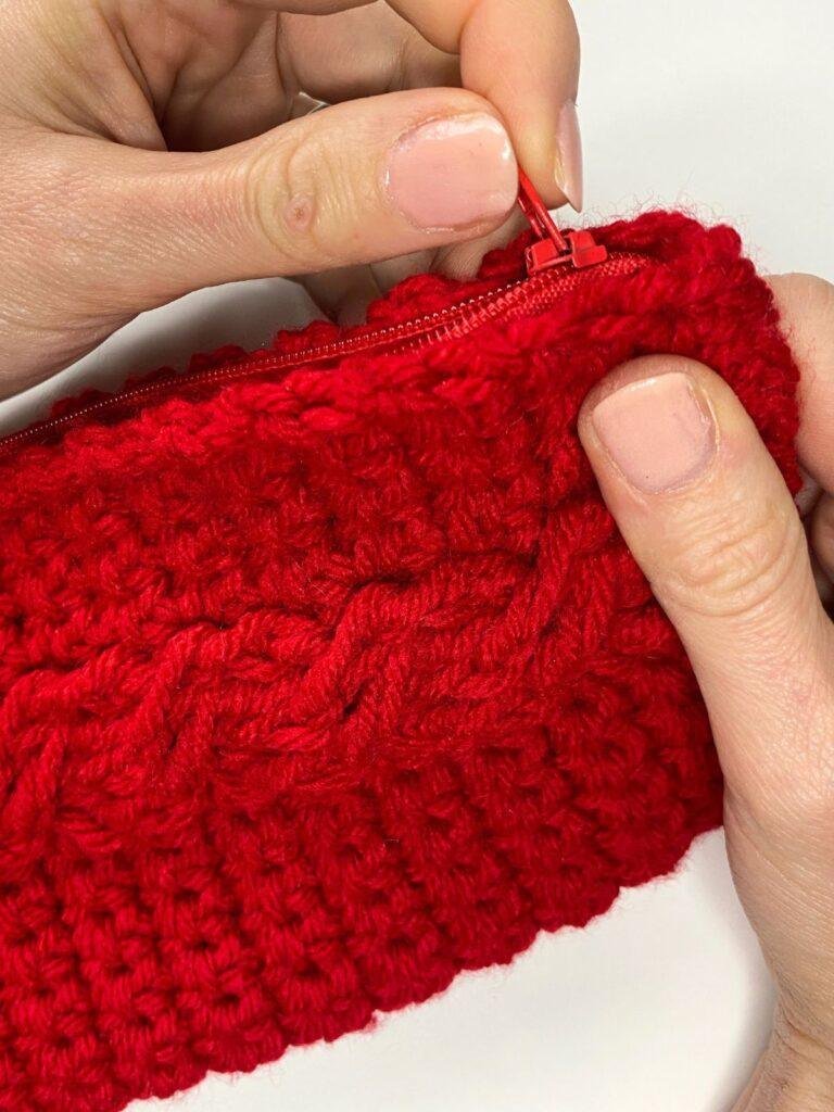 A person's hands zipping up a red crochet case