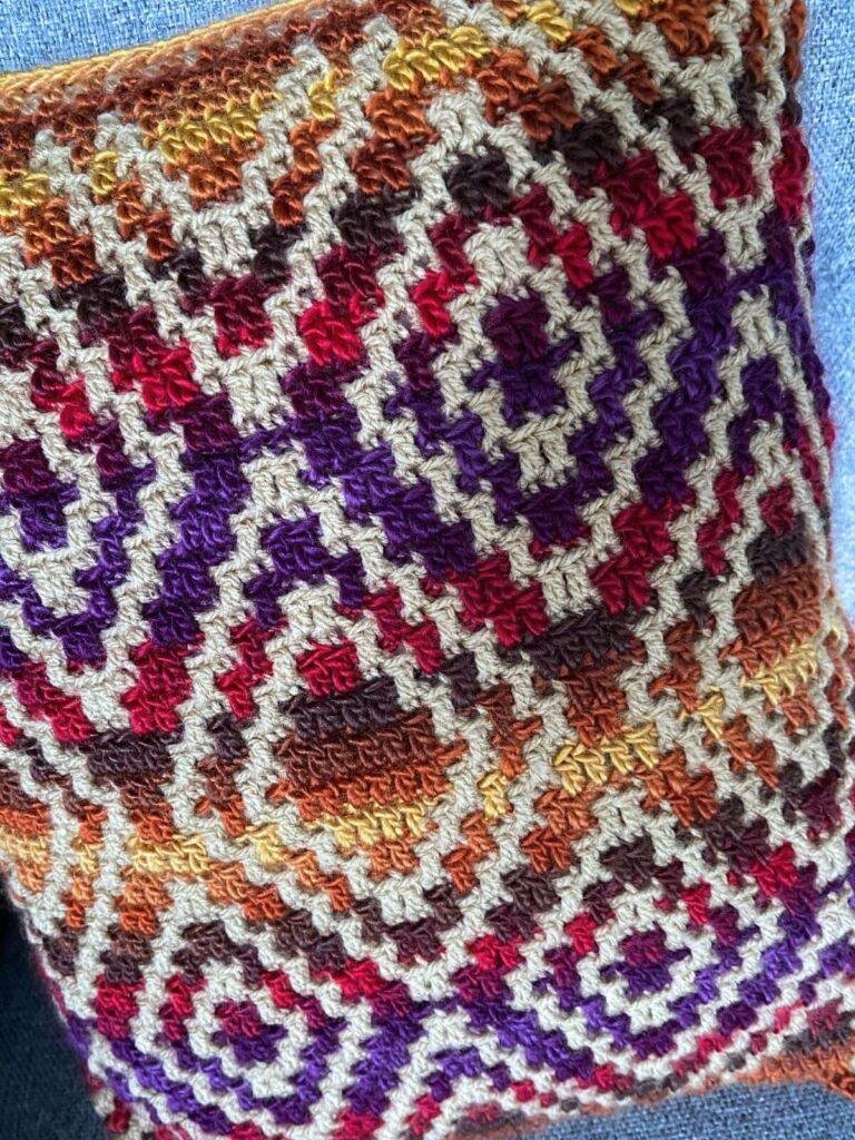 close up of a diamond pattern crochet pillow in multi-coloured yarn