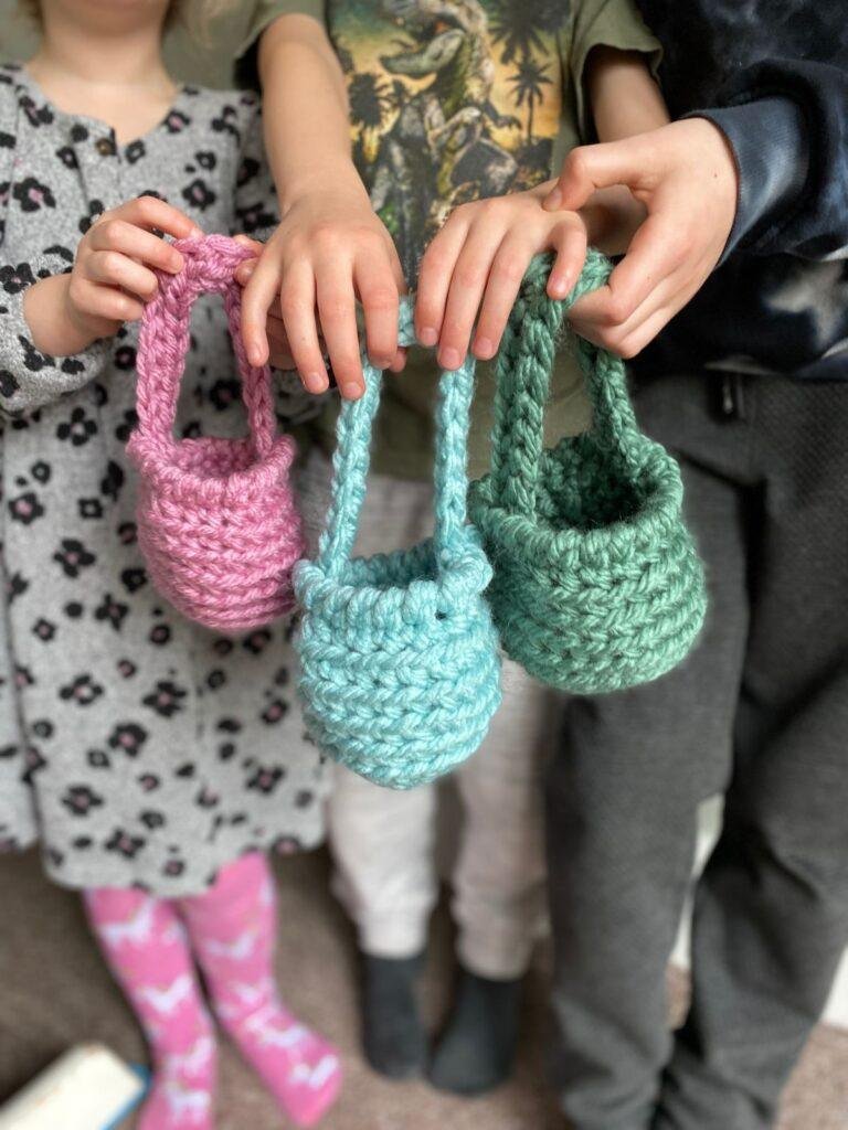 3 children are standing holding 3 crochet easter baskets