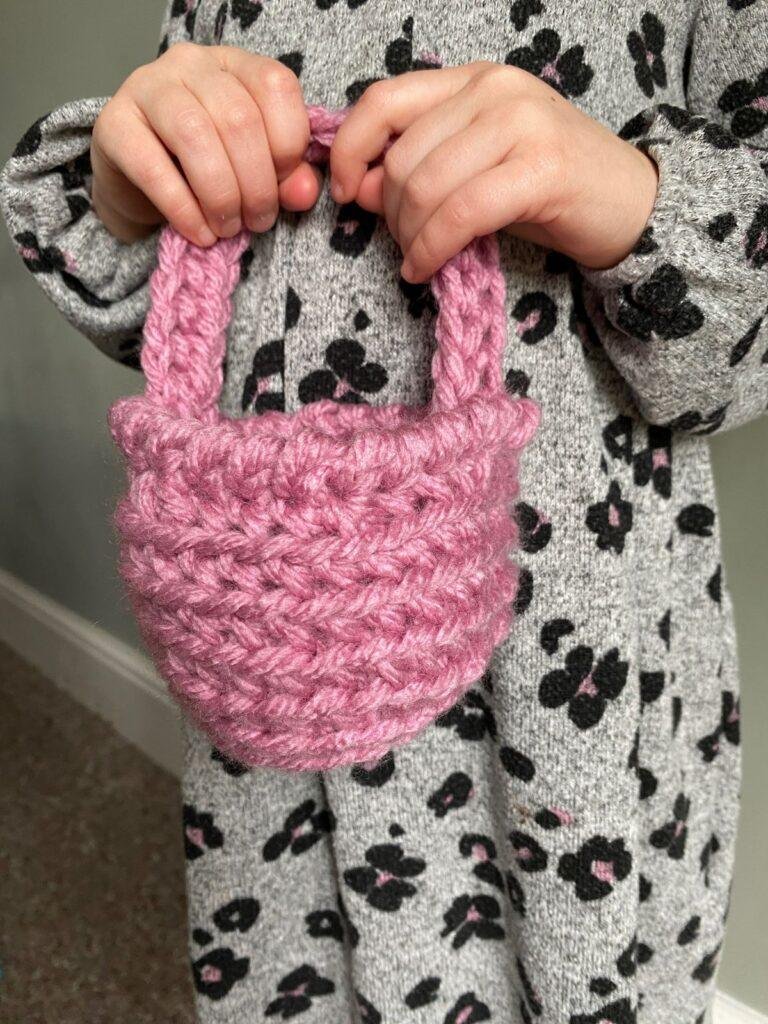 A girl in animal print dress holds a pink crochet basket in both hands