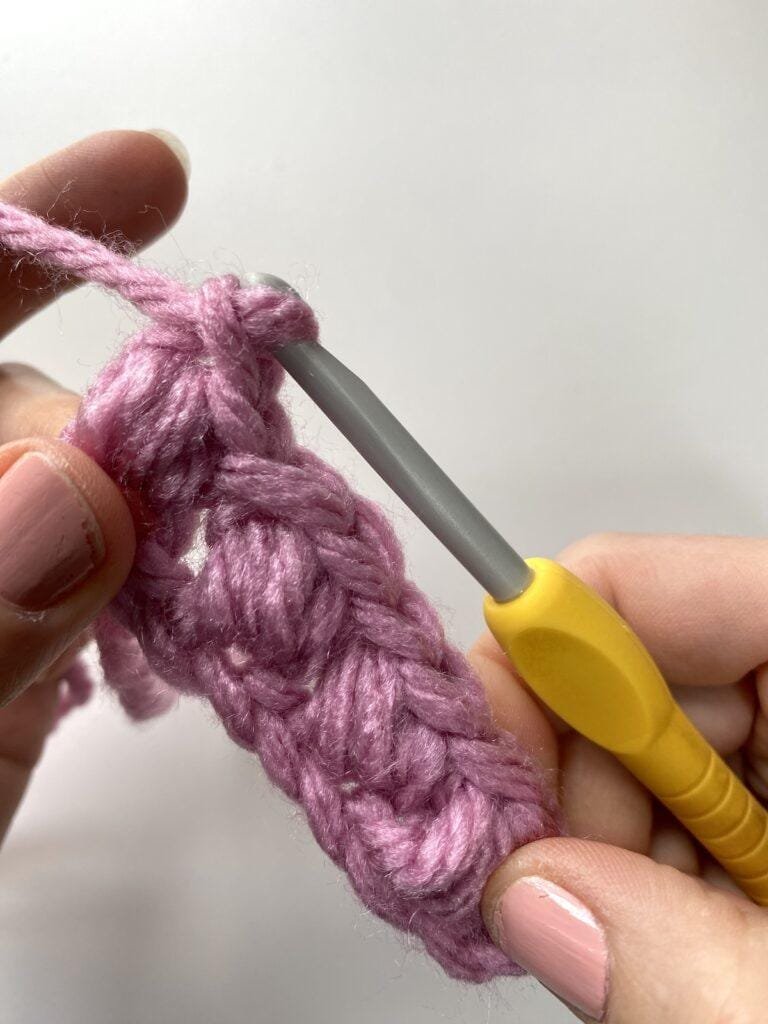 a row of crochet bean stitches showing an extra chain 1 at the end of a row with a yellow hook