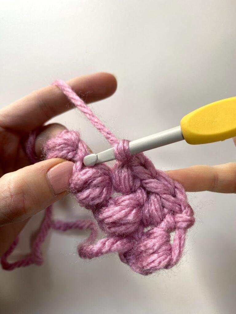 A crochet hook is showing where to place a bean stitch in a row of pink fabric