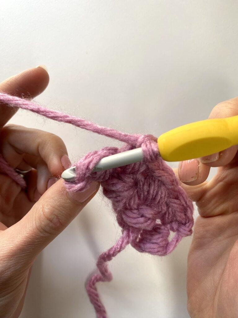 A crocheter is crocheting a row with pink yarn