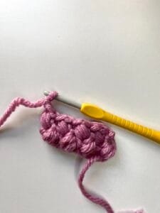 A completed sample of the crochet bean stitch in pink yarn with a yellow hook