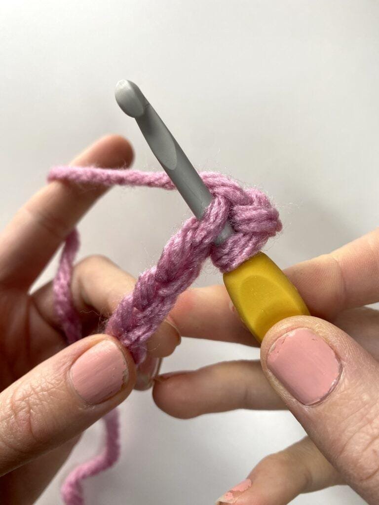 2 hands insert a crochet hook into a chain of yarn
