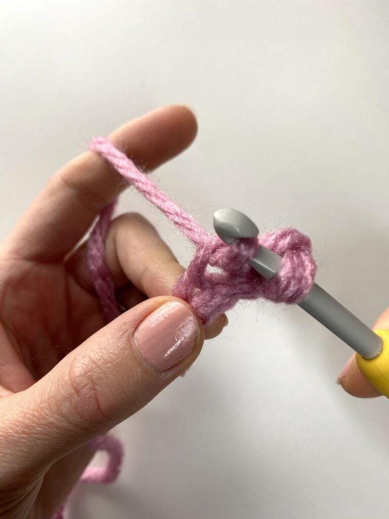 2 hands are crocheting with pink yarn and a yellow hook
