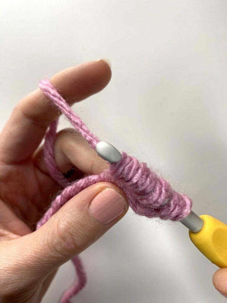a crochet hook with 4 loops on it held by a hand
