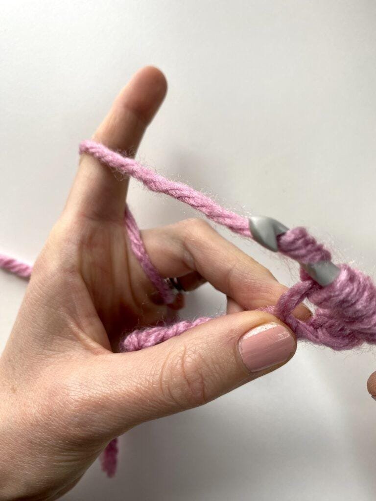 a hand holding yarn and making a crochet stitch