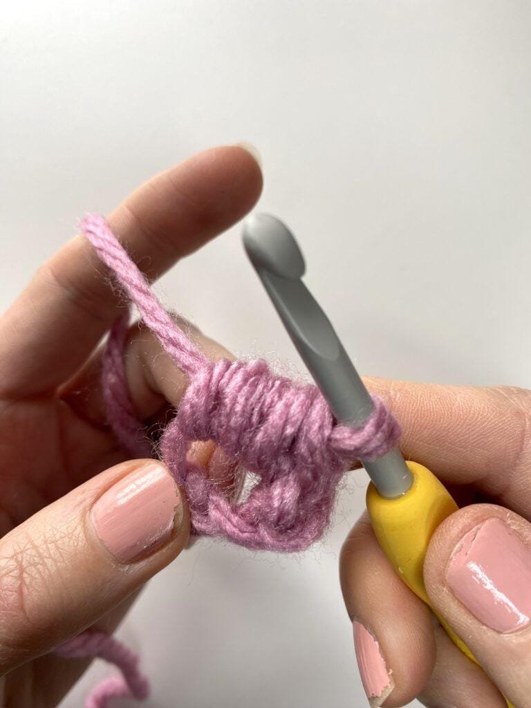 A crochet bean stitch has just been completed by the hand holding it and a yellow crochet hook