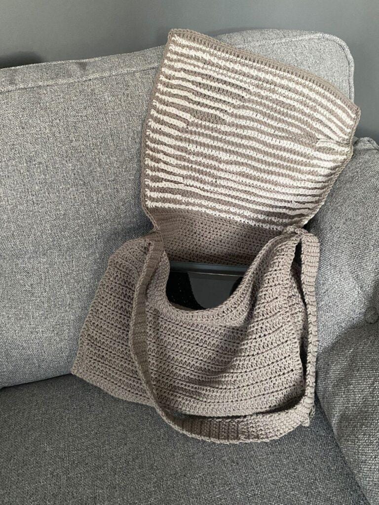 An open crochet messenger bag sits open on a grey sofa