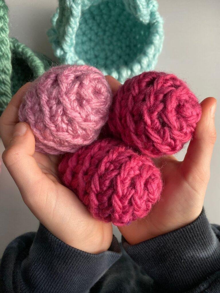 2 hands holding 3 crochet easter eggs in pink with a basket behind