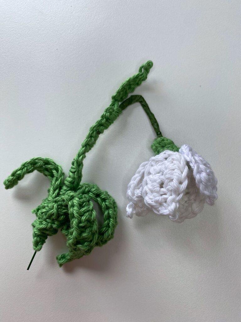 A single crochet snowdrop lays on a white surface