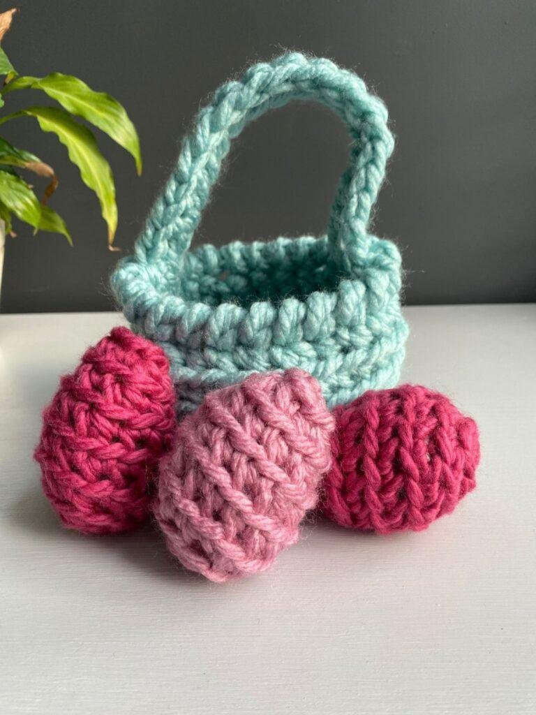 3 pink easter eggs in front of a blue crochet treat basket