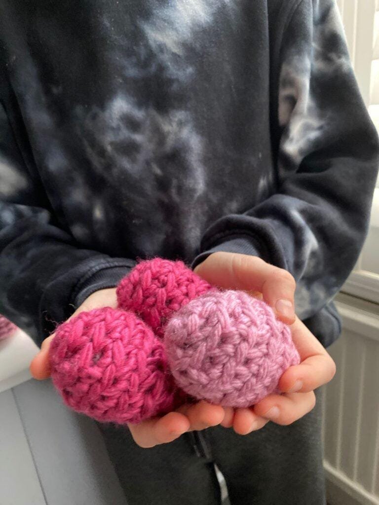 A person in a black tie dye top holds 3 pink crochet eggs