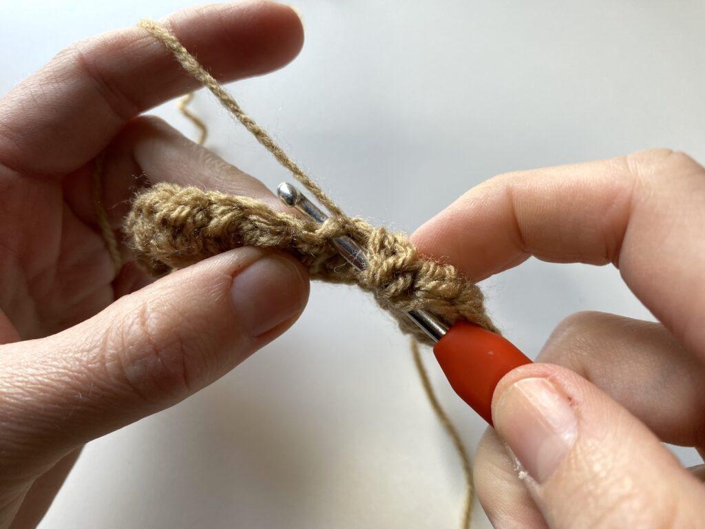 step 2 of the crochet pique stitch is shown here with an orange hook and beige yarn