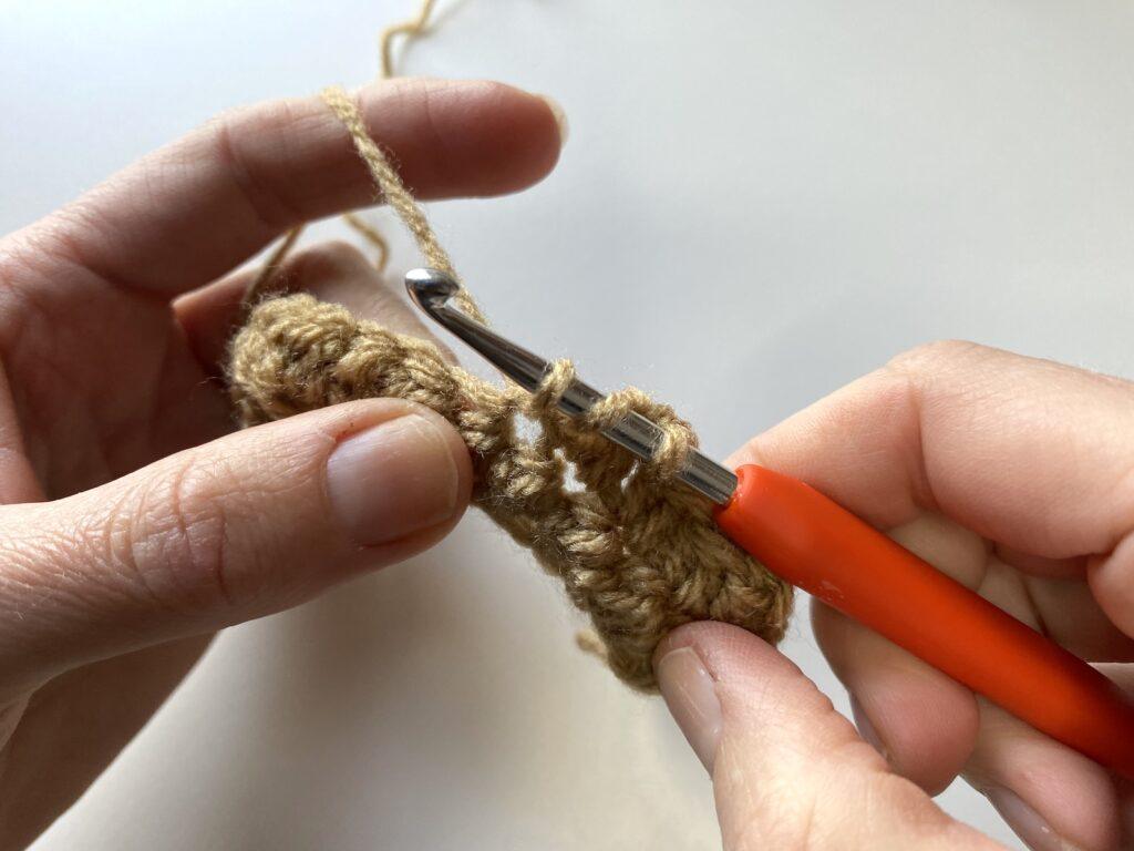 a person is showing step 3 of the crochet pique stitch with beige yarn
