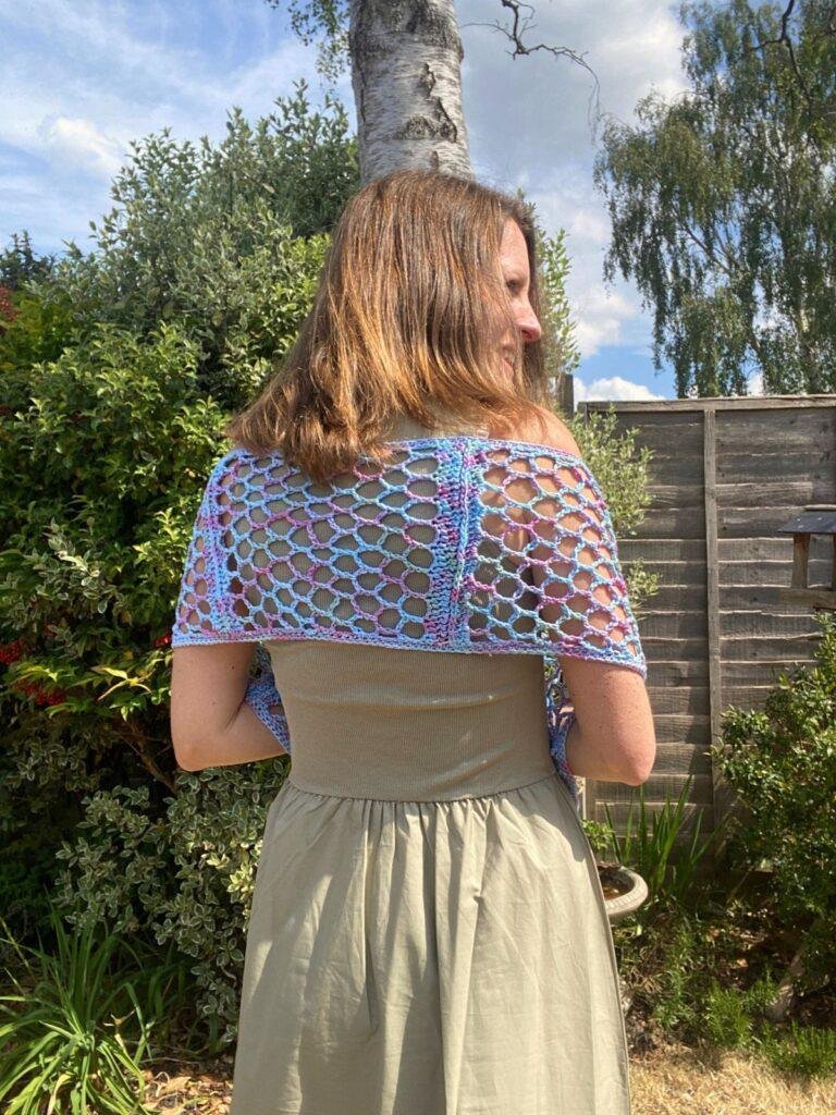 A woman stands in a garden wearing a green dress and an ocean coloured crochet lace scarf