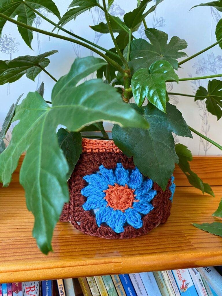 A crochet plant holder has a plant in it sitting on a shelf