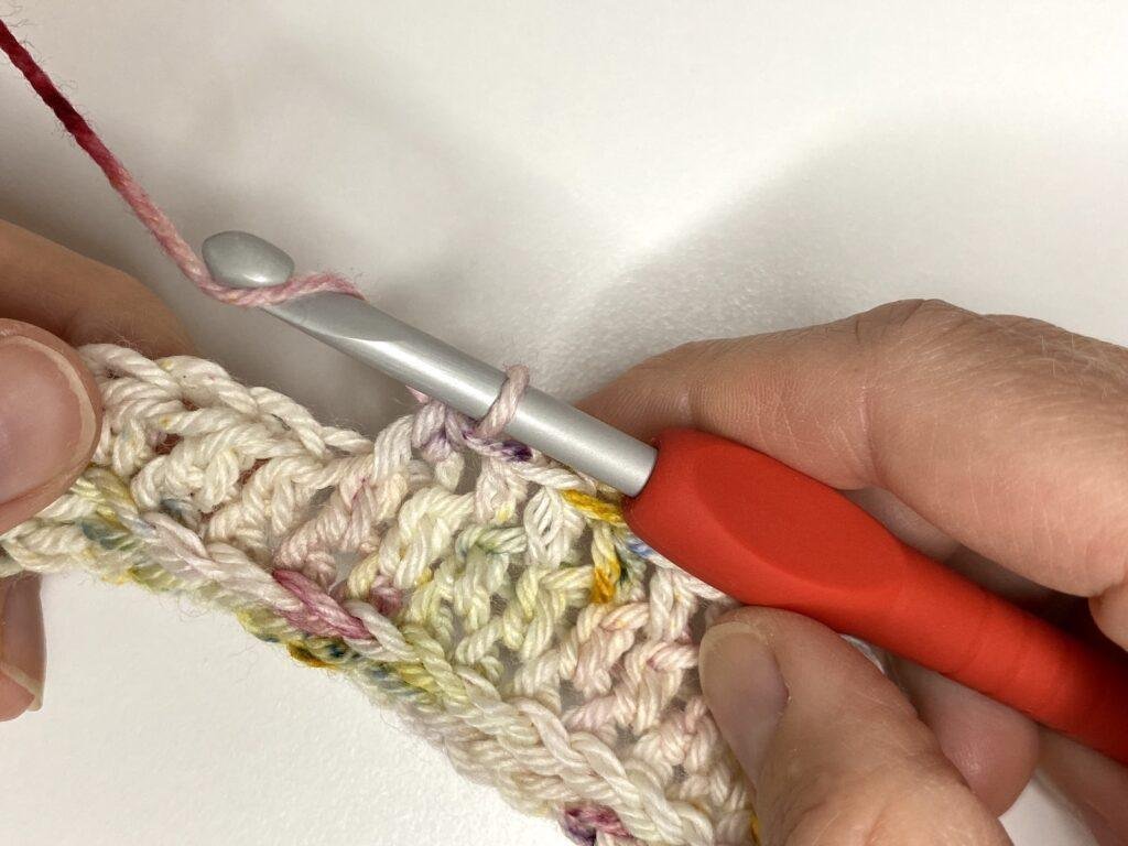 2 hands are crocheting by wrapping the yarn around the hook