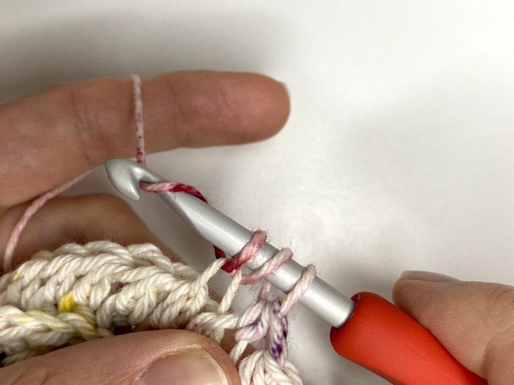 A person is wrapping the yarn over the hook with 3 loops already on the hook in a crochet stitch