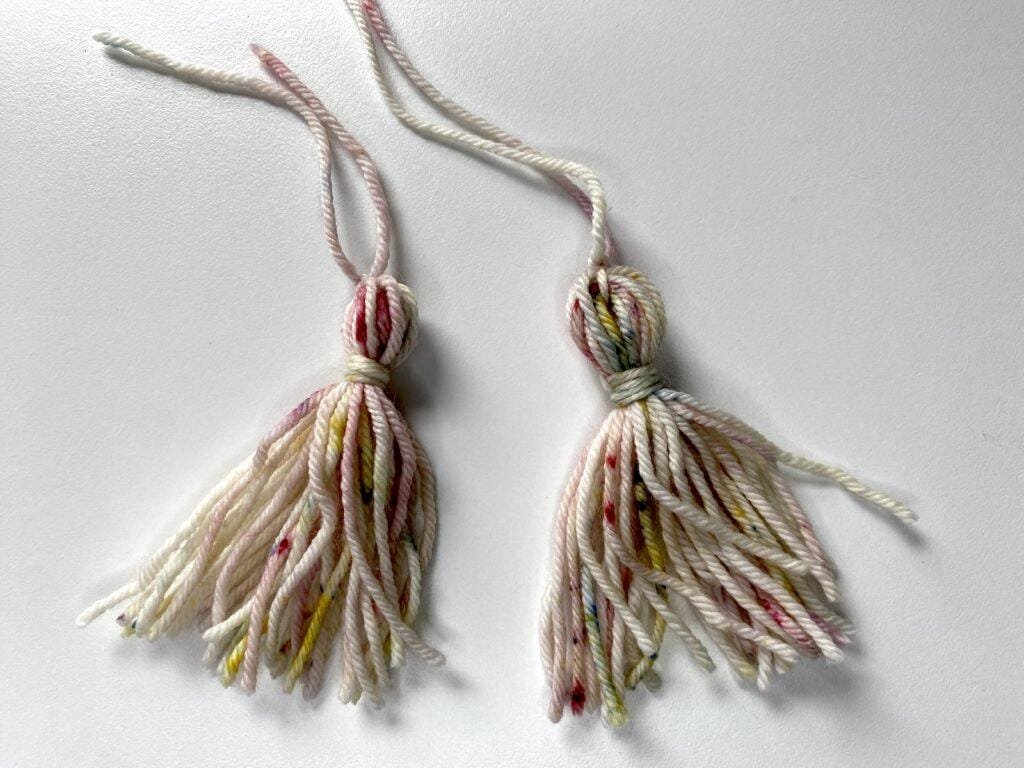 2 tassels made out of multi-coloured yarn on a white background