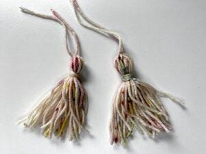 2 tassels made out of multi-coloured yarn on a white background