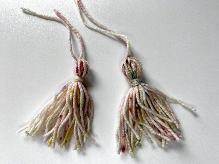 2 tassels made out of multi-coloured yarn on a white background