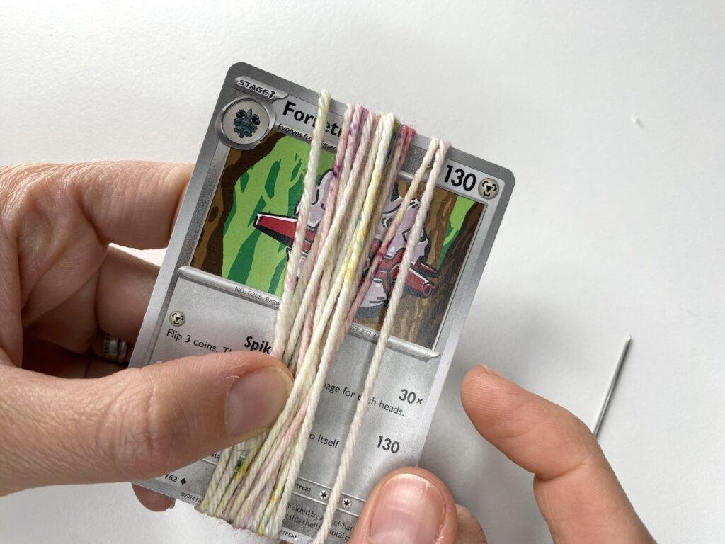 A lady holds a pokemon card with yarn wrapped around it