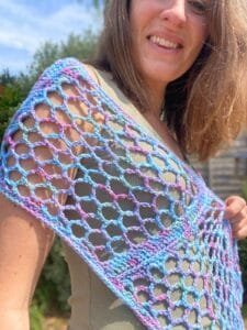 A lady is smiling ad wearing a blue and pink variegated lace scarf around her shoulders