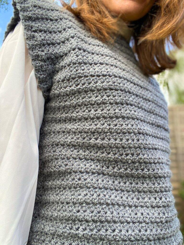 A close up of a textured crochet sleeveless top worn by a person