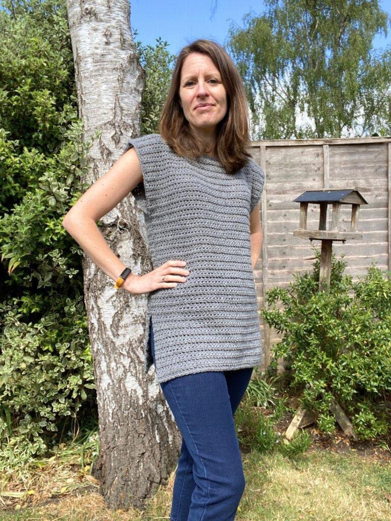 A lady wears jeans and a crochet tunic in a sunny garden