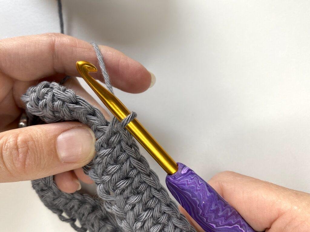 A completed waistcoat stitch working in the round on a piece of grey crochet fabric with a purple hook