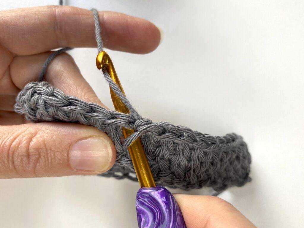 A person wrapping the yarn over the hook as part of the knit stitch