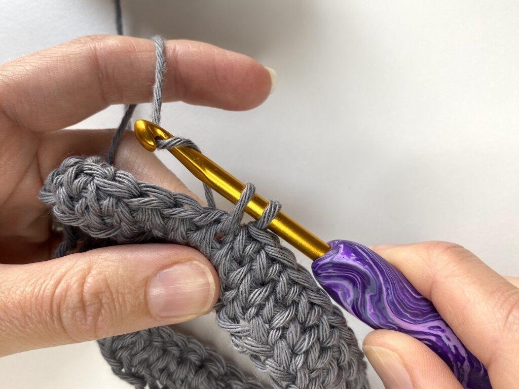 a person wrapping the yarn around the hook, whilst making a crochet knit stitch