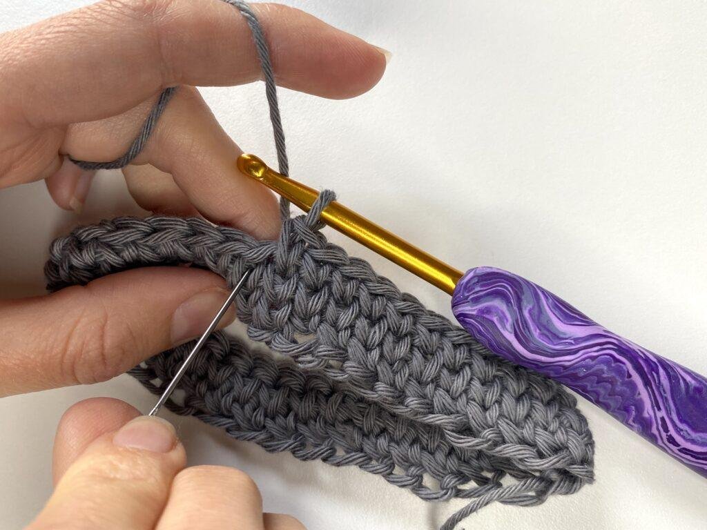 A person using a needle to point to the place where you insert your hook for crochet waistcoat stitch in the round