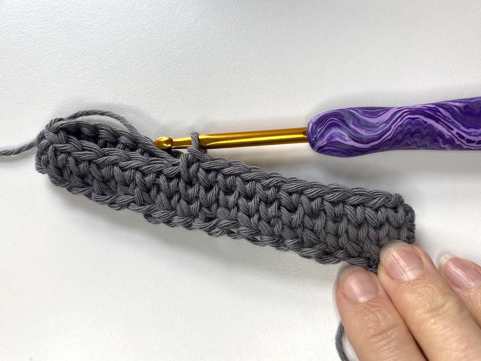 A grey sample of crochet waistcoat stitch in the round with a purple crochet hook