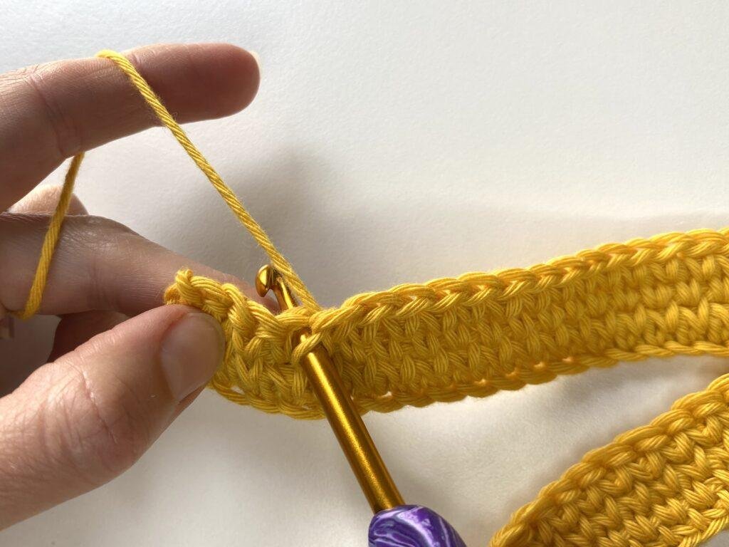 A crochet hook has been inserted into a stitch in a yellow piece of crochet 