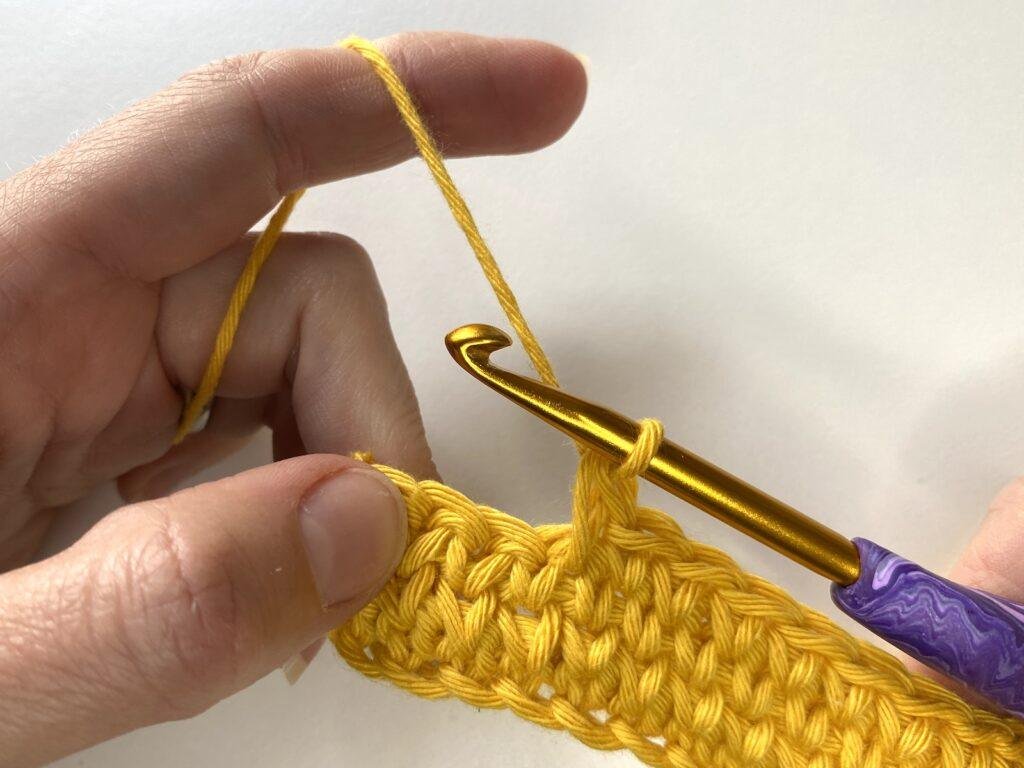 2 hands holding a piece of crochet fabric and a completed stitch