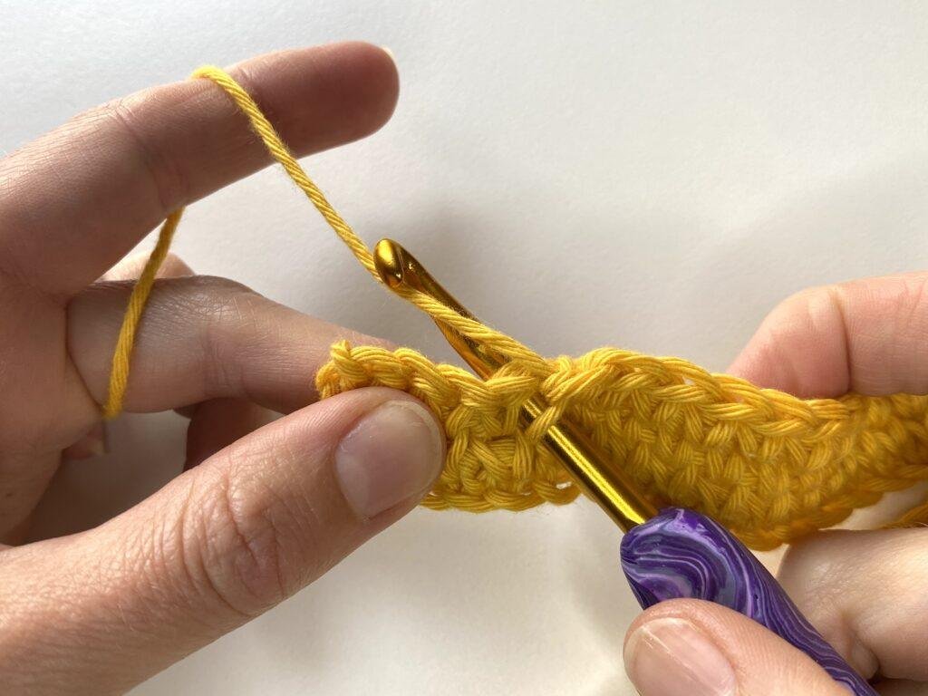 The yarn is wrapped around the hook partway through a waistcoat crochet stitch