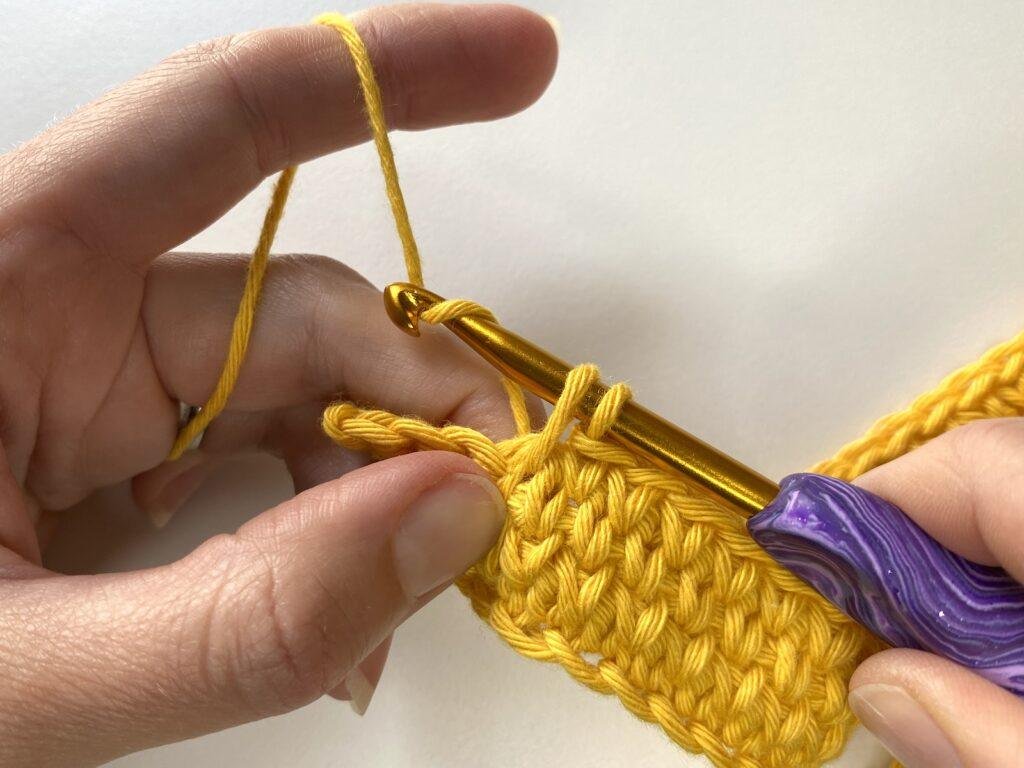 a person crocheting with yellow yarn showing their hands and a purple hook
