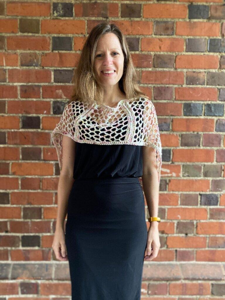 A lady wearing a black dress with a lacy white with specks of colour crochet shawl, perfect for a wedding outfit