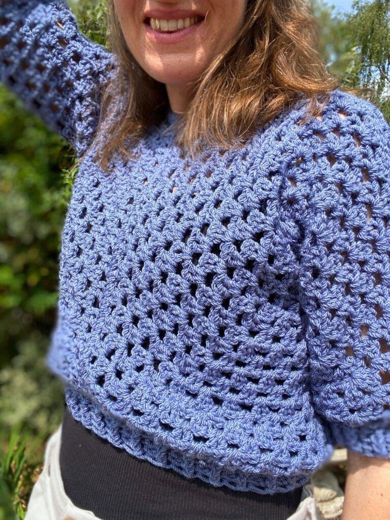 A close up of a person wearing a crochet cropped sweater in blue