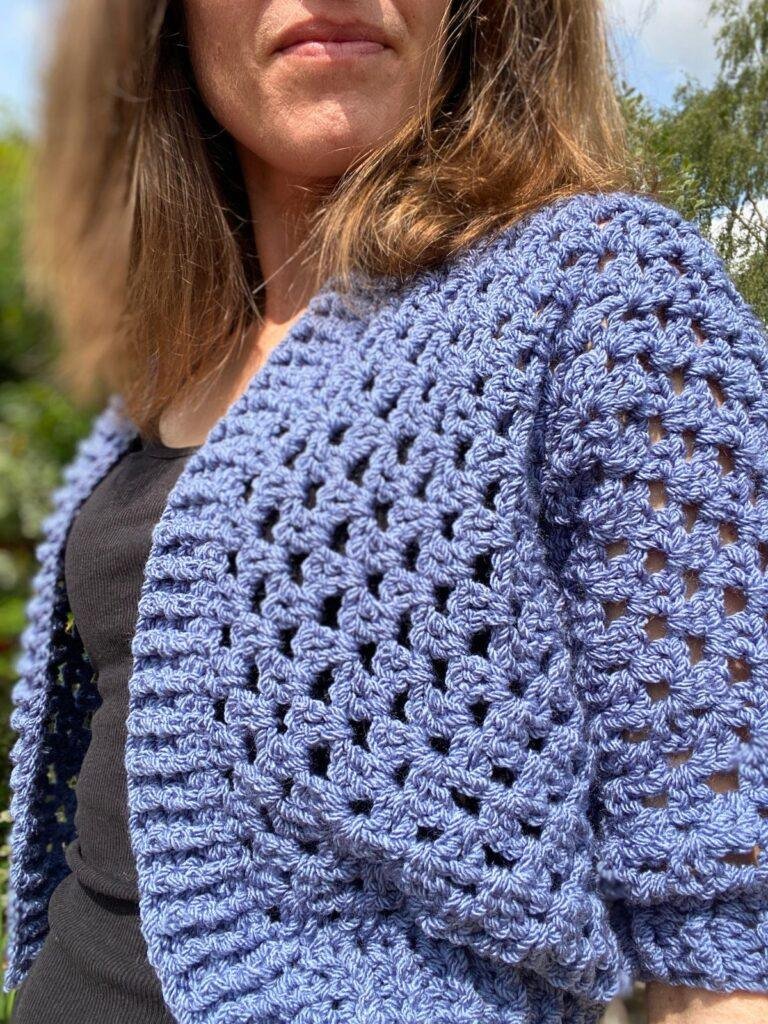A close up of a person wearing a crochet lace stitch cardigan with ribbing down the front
