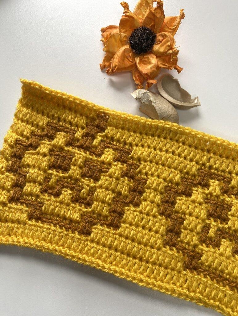 A mosaic crochet pumpkin pattern laid at an angle with an orange flower above