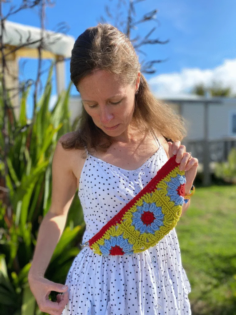 A lady stands outside in the sunshine looking down at a bright granny square crossbody bag