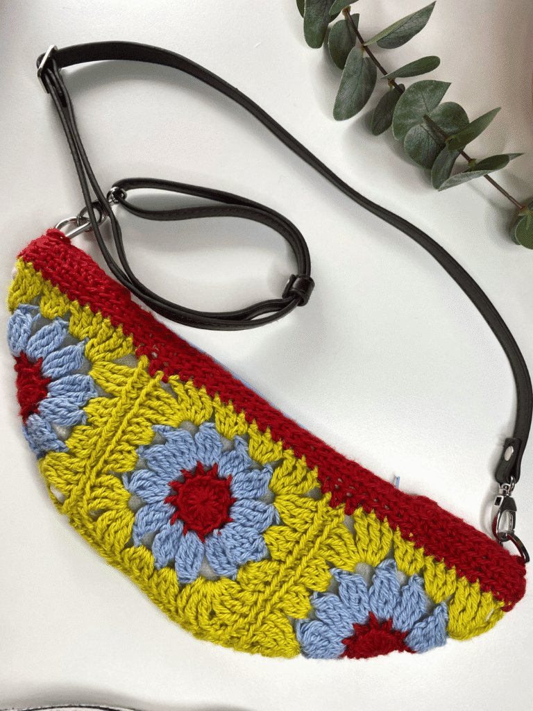 A flat lay image of a crochet bag with flower motifs in yellow, blue and red.