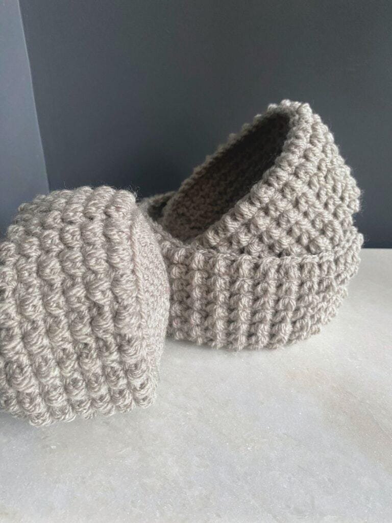 3 crochet basket made of grey yarn with bobbles all over, are arranged with one inside the other and the third on its side