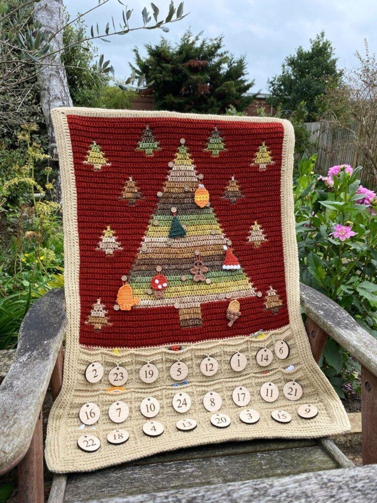 A crochet Christmas tree advent calendar is laid over a chair in a garden