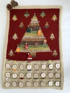 A crochet advent calendar with a Christmas tree, pockets underneath and hanging decorations on the tree