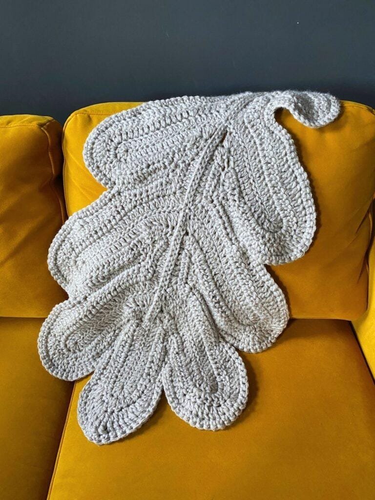 An oak leaf blanket is lain over a yellow sofa